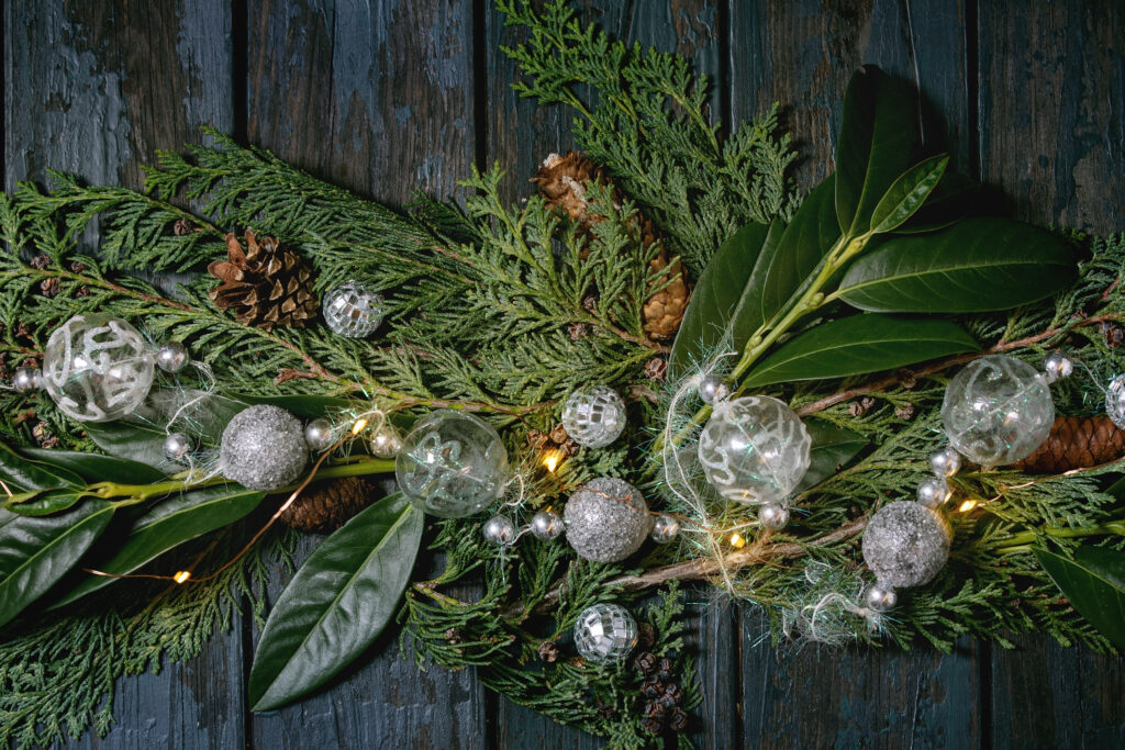 Wintery greens on top of table with holiday ornaments, decorations and lighting